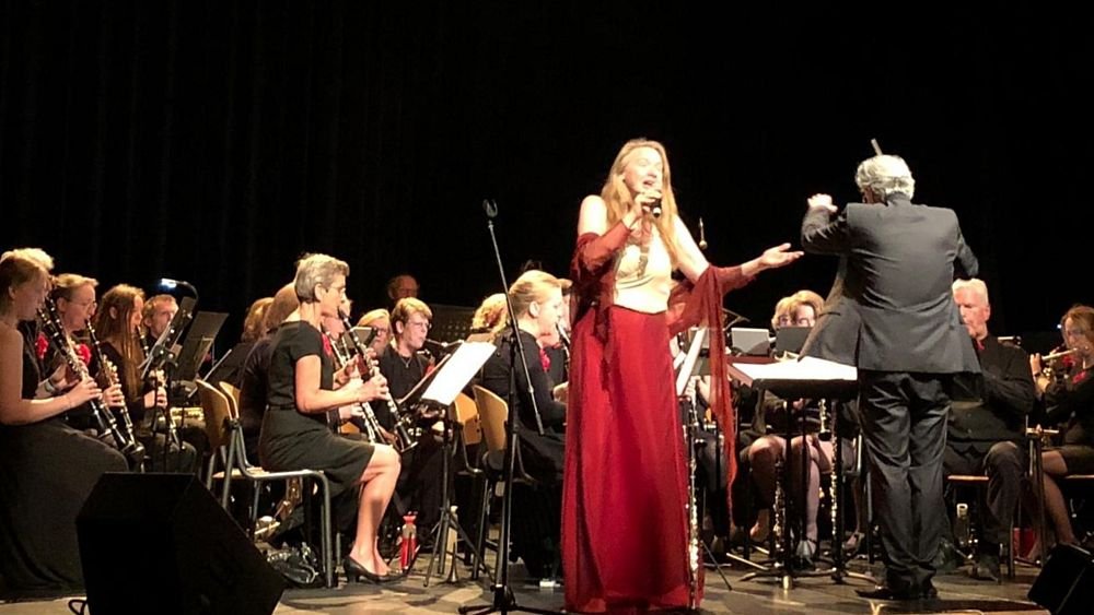 Op de voorgrond zangeres Micheline Van Hautem en (op de rug) Willem van Zee, met daar achter Groot Harmonieorkest Crescendo. Foto: @deteyding (zie enkele tweets verderop)